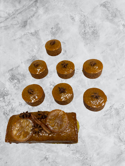 Cake pain d'épices, décoré avec des oranges confit, des bâtons de cannelles sur un fond de marbre blanc