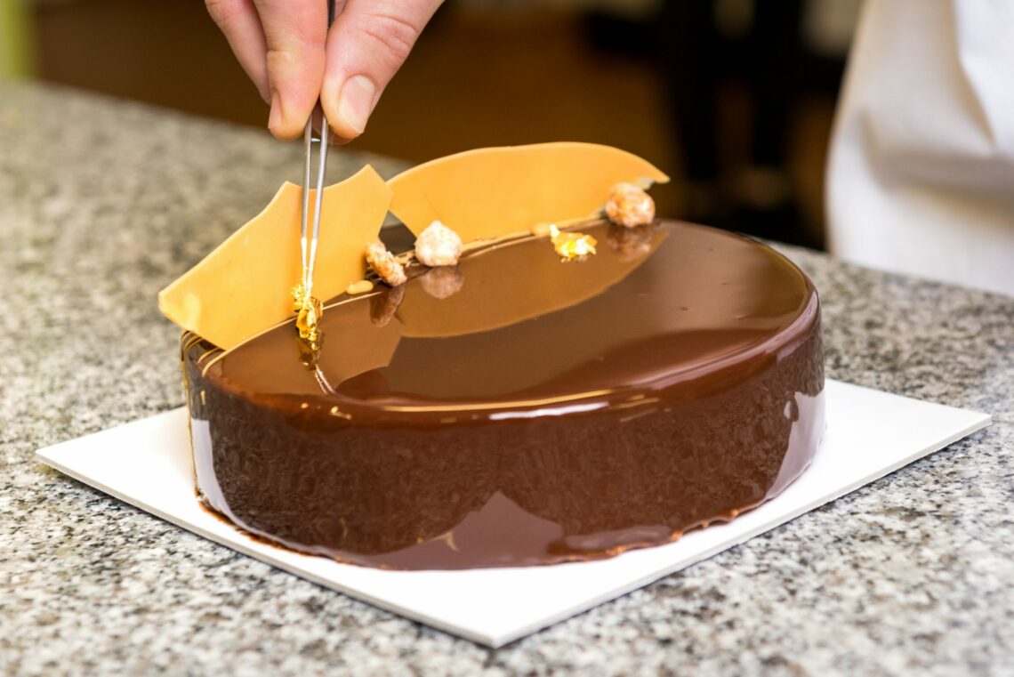 Entremet glacé en couloir chocolat lait, décoré de coraux de chocolat dulcey, étant entrain d'être décoré avec des feuilles d'or et des fruits caramélisés